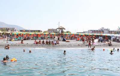 Spiaggia affollata con persone e file di ombrelloni colorati.