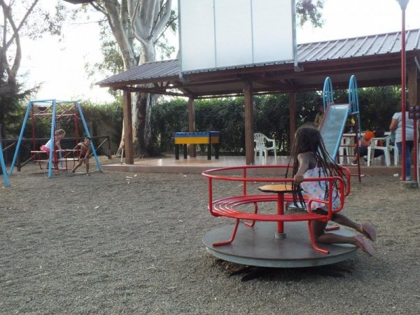 Parco giochi con bimbi su giostra, altalene, e scivolo.