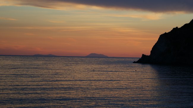 Tramonto sul mare con silhouette di una scogliera.