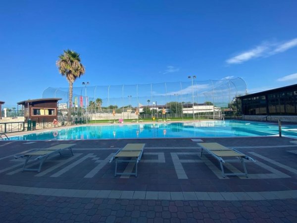 Piscina all'aperto con lettini, palme e cielo azzurro.