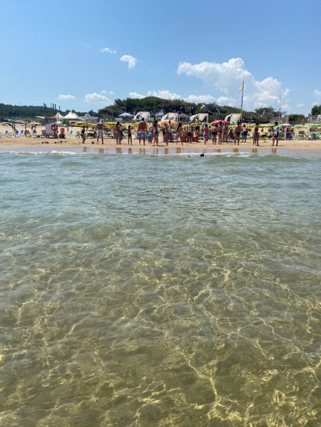 Vista del mare limpido verso una spiaggia affollata con ombrelloni e gente.