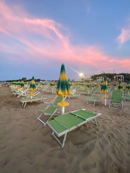 Ombrelloni verdi e gialli chiusi su una spiaggia al tramonto con cielo rosa.