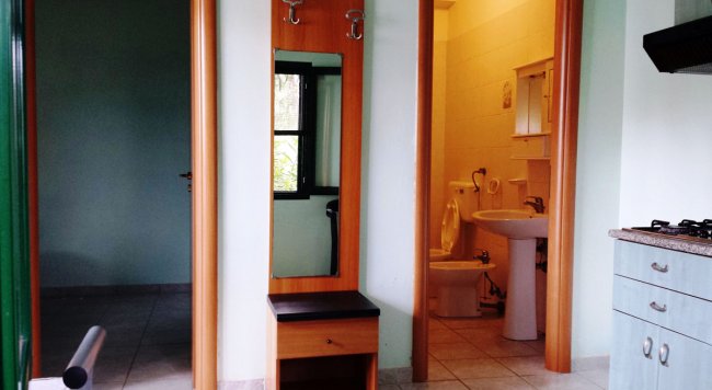 Corridoio con specchio e appendiabiti, porta verso bagno con wc e lavandino visibili.