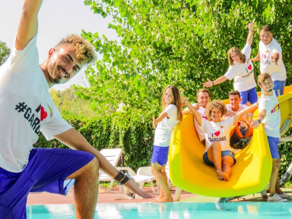 Persone sorridenti su uno scivolo giallo vicino a una piscina.
