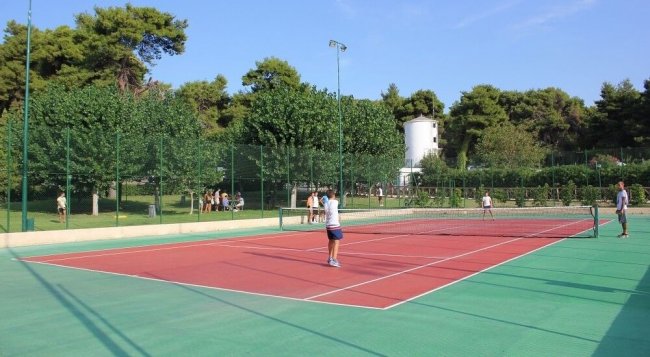 Persone giocano a tennis su un campo rosso.