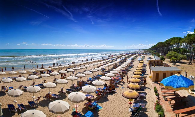 Spiaggia con file di ombrelloni e lettini, mare calmo e cielo blu.
