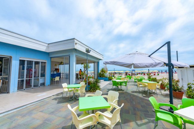 Terrazza esterna con tavoli colorati e vista sulla spiaggia.