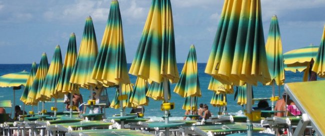 Ombrelloni a righe verdi e gialle su una spiaggia affollata con il mare sullo sfondo.