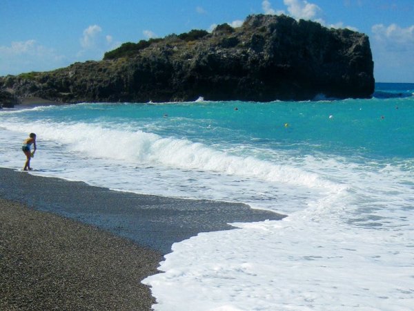Bambino gioca sulla spiaggia di ciottoli con onde che si infrangono.