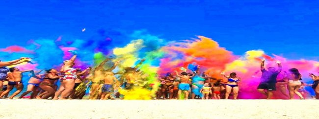 Gruppo di persone lancia polveri colorate su una spiaggia.