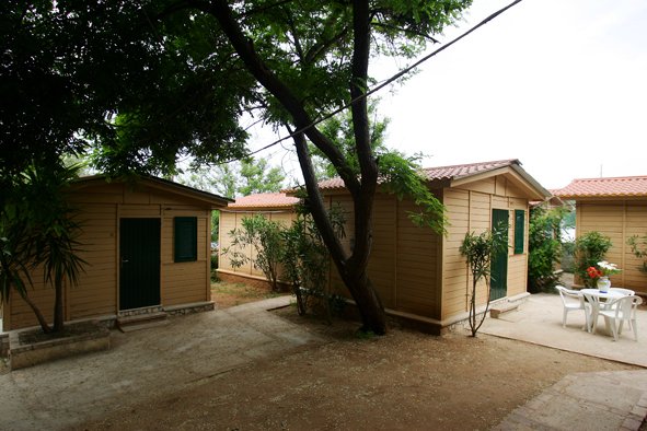 Esterno di bungalow in legno con tavolo e sedie, alberi e arbusti.