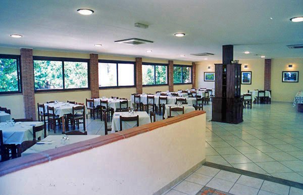 Sala da pranzo luminosa con tavoli apparecchiati, pareti vetrate e pavimento piastrellato.