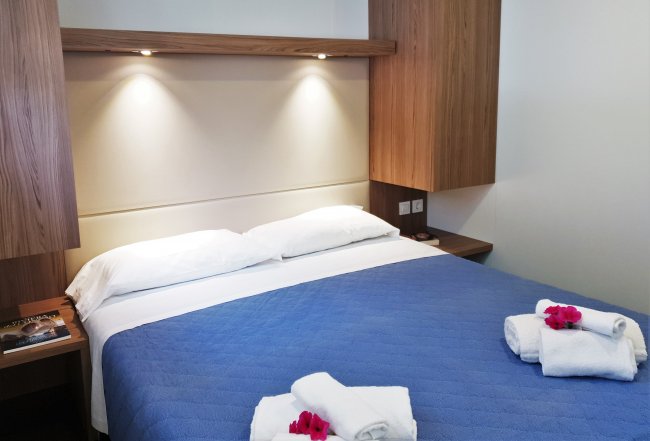 Letto con copriletto blu, asciugamani arrotolati, fiori rossi.