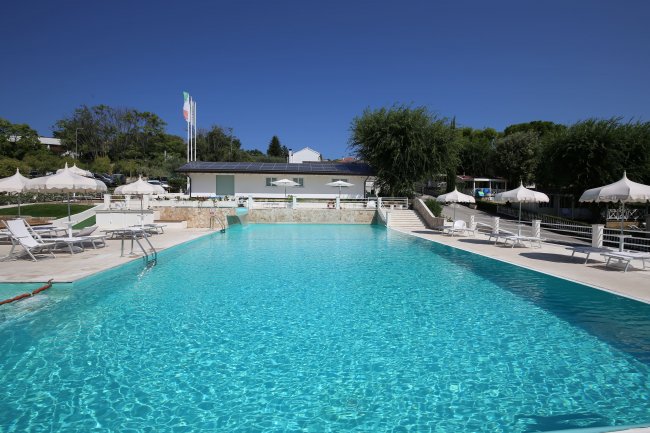 Piscina azzurra con lettini e ombrelloni bianchi, cielo limpido.