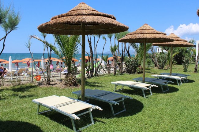 Lettini sotto ombrelloni di paglia su un prato con vista sul mare.