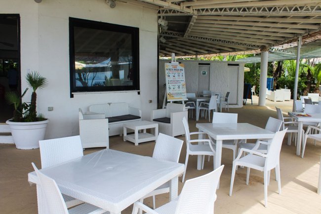 Area esterna di un bar con sedie e tavoli bianchi.