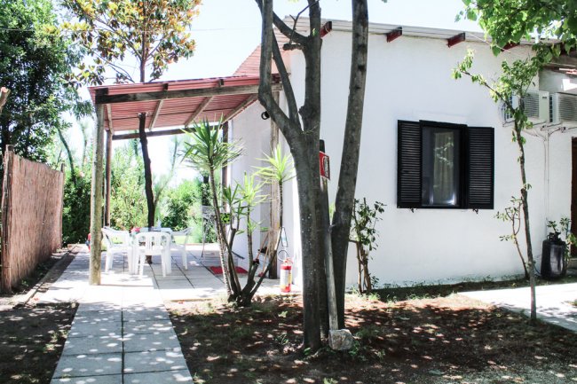 Una piccola casa bianca con veranda e tavolo esterno circondata da alberi.