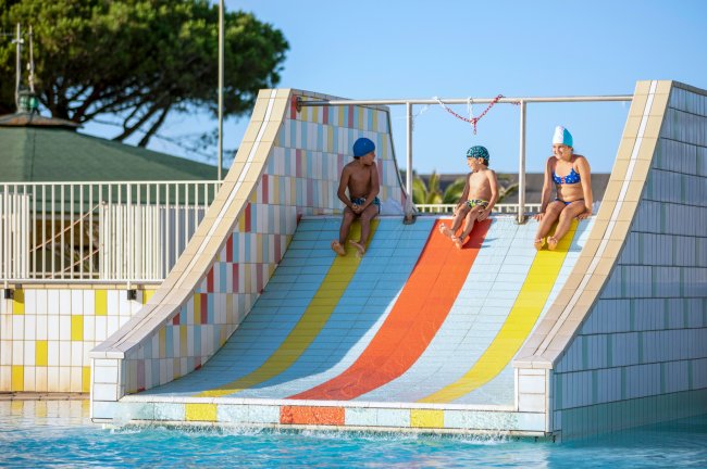 Tre bambini scendono uno scivolo colorato in piscina.