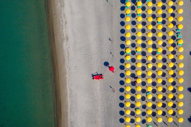 Ombrelloni gialli allineati su una spiaggia sabbiosa vista dall'alto.