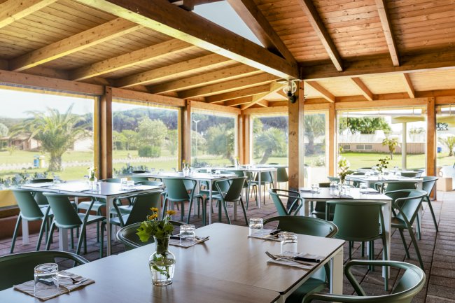 Sala da pranzo con tavoli apparecchiati e vista sul giardino.