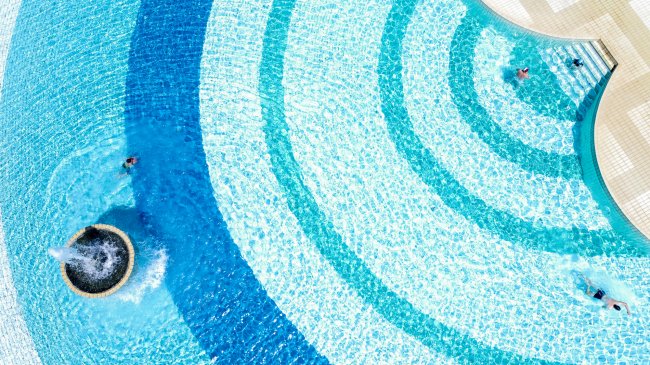 Vista dall'alto di una piscina con motivi ad arco e persone che nuotano.