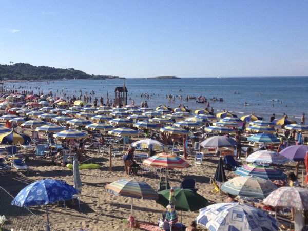 Spiaggia affollata con ombrelloni colorati e persone che nuotano nel mare.