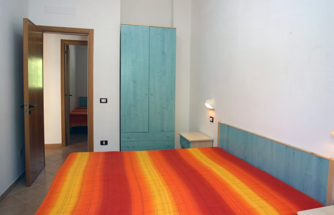 Camera con letto matrimoniale, coperta arancione, armadio azzurro e porta aperta.