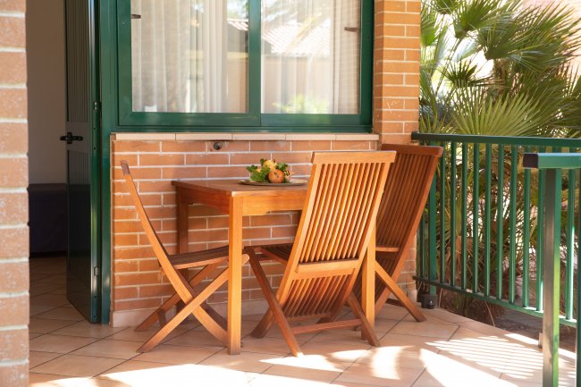 Tavolo in legno con due sedie su un balcone piastrellato.