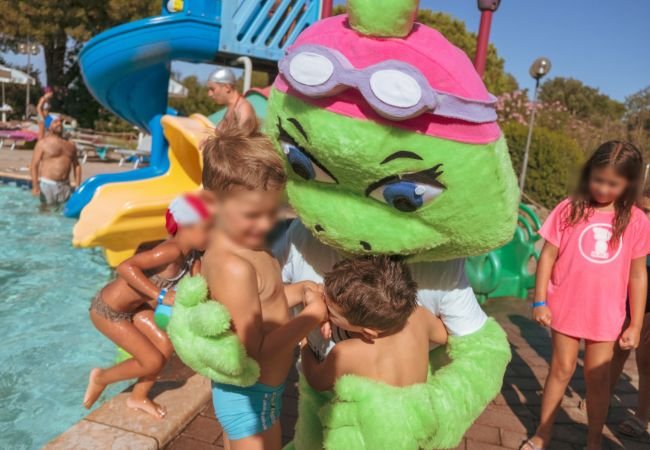 Mascotte verde abbraccia bambini vicino a uno scivolo d'acqua.