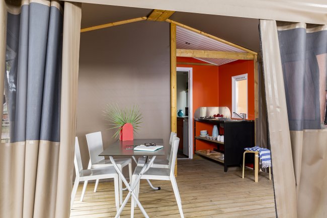 Interno di una tenda con tavolo e sedie, cucina in fondo.