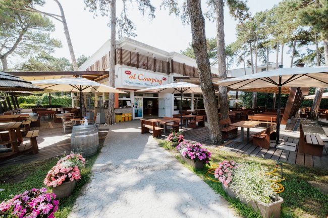Un ristorante all'aperto tra gli alberi con tavoli di legno e fiori colorati.