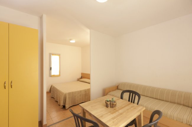 Vista su una stanza con tavolo, sedie, divano e letto in secondo piano.
