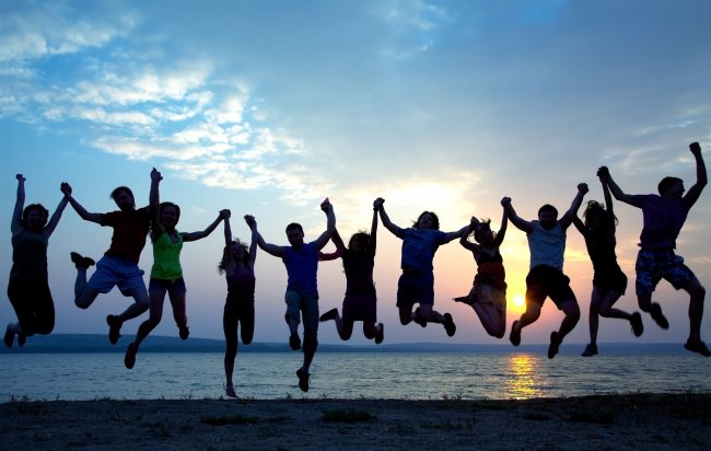 Persone che saltano tenendosi per mano al tramonto su una spiaggia.