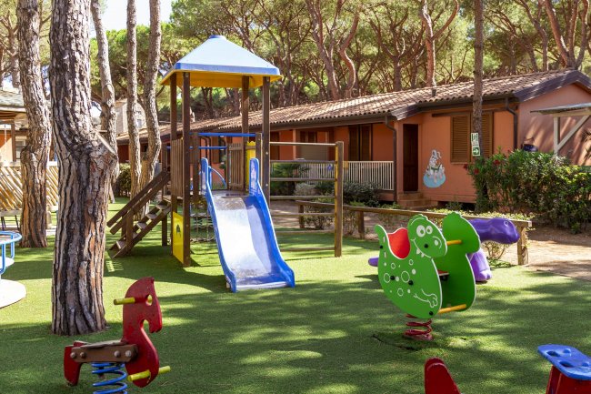 Parco giochi con scivolo blu e giochi a molla su erba sintetica.