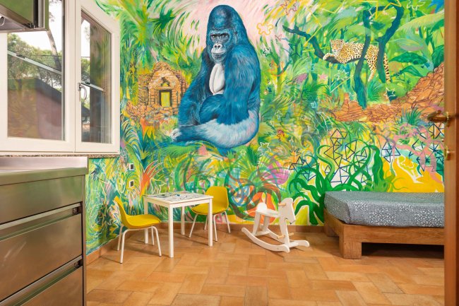 Stanza colorata con murale di giungla e gorilla, tavolino e sedia per bambini.