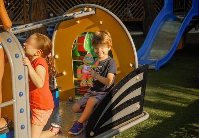 Due bambini giocano su una struttura in un parco giochi; uno tiene un giocattolo.