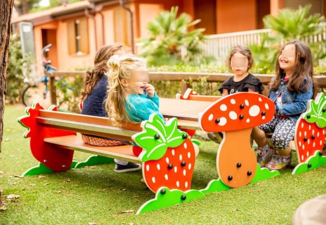 Bambini seduti a un tavolo da picnic con decorazioni di fragole e funghi in un parco giochi.