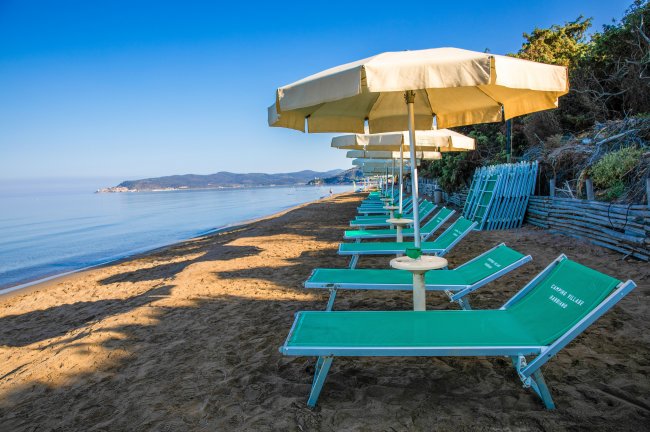 Una spiaggia con lettini verdi e ombrelloni gialli allineati lungo la riva.