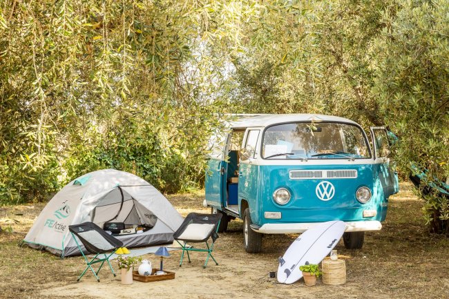 Furgone Volkswagen con tenda e attrezzatura da campeggio in un boschetto.