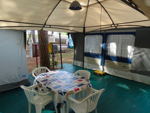 Interno di una veranda con tavolo coperto da tovaglia e sedie in plastica bianca.