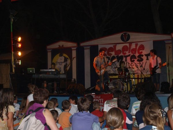 Concerto serale all'aperto con band sul palco e pubblico seduto.