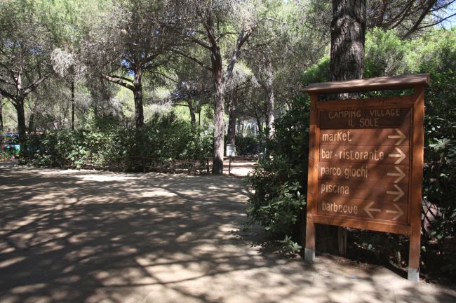 Insegna in un campeggio tra alberi e sentieri ombreggiati.
