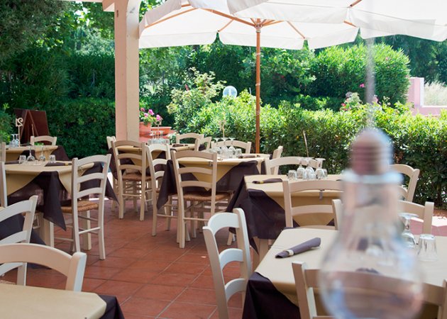 Terrazza di un ristorante con tavoli apparecchiati, circondata dal verde.