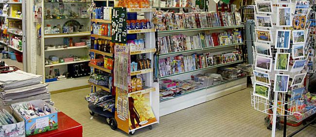 Interno di un negozio con scaffali di riviste, snack e cartoline.