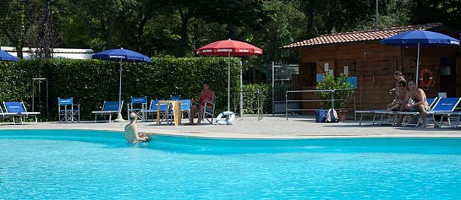 Una piscina circondata da lettini e ombrelloni, con alcune persone a bordo vasca.