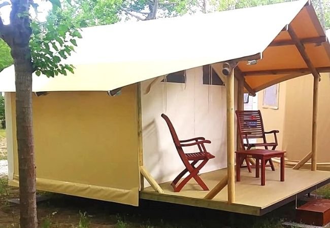 Una tenda con due sedie su una veranda in legno, circondata da alberi.