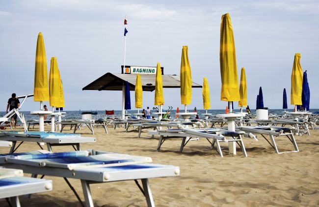 Una spiaggia con lettini e ombrelloni gialli e blu chiusi, vicino al mare.