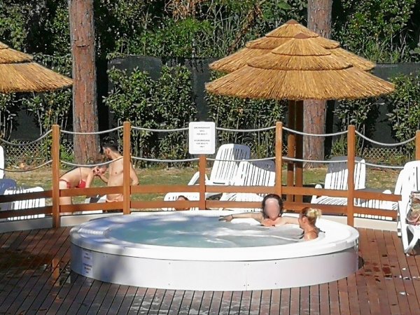 Persone rilassate in una vasca idromassaggio all'aperto su una terrazza in legno.