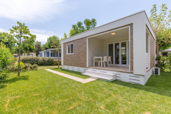 Unità abitativa moderna con veranda nel verde e sentiero d’ingresso.