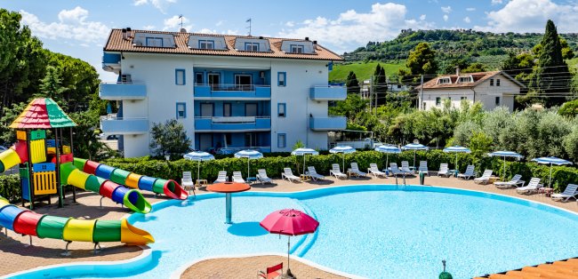 Una piscina con scivoli colorati, sedie a sdraio e un edificio residenziale sullo sfondo.